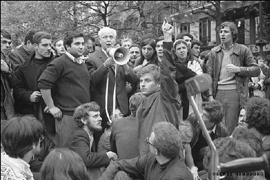 Student leader Daniel Cohn-Bendit raises his arm for silence to allow poet Louis Aragon to talk to students on a megaphone. [Photo by Serge Hambourg/via NPR]